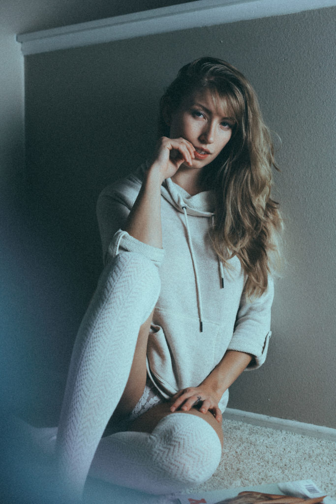 Color photo of Verronica Kirei sitting on the floor wearing white sweater and white socks.